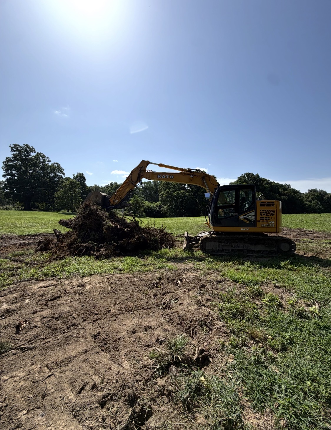 Excavator lifting a large stump and roots from a field