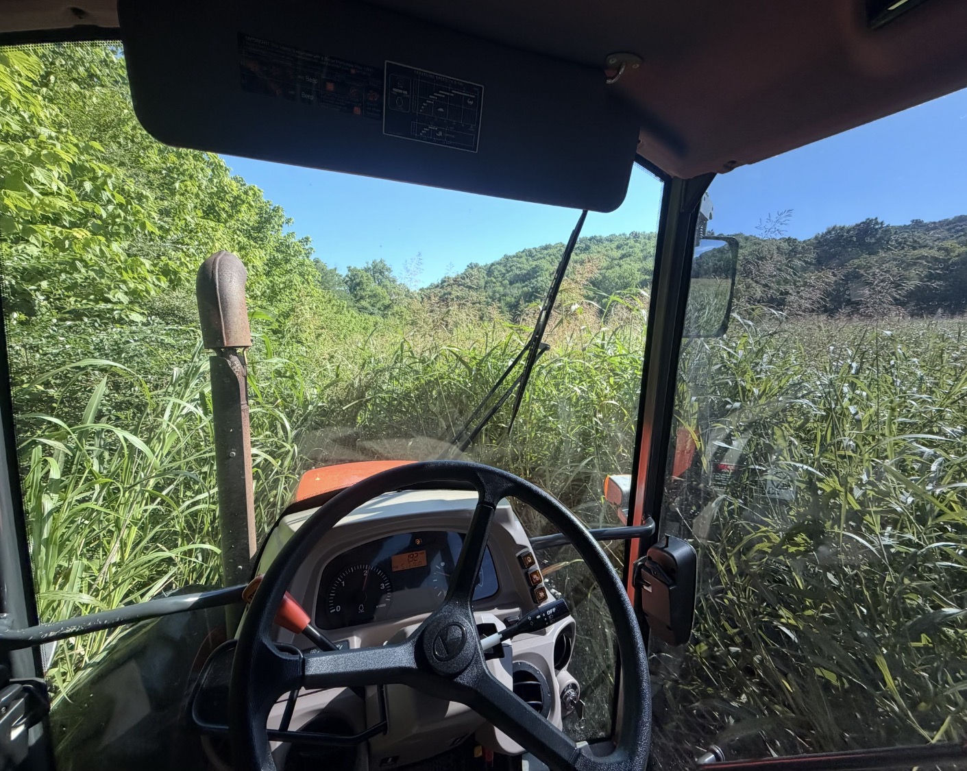 Tractor cutting through tall grass seen from inside the cab