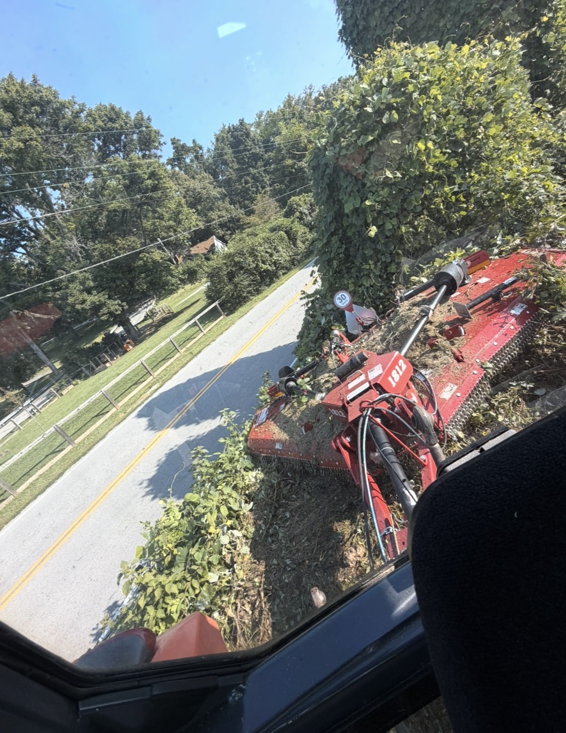 Brush hog cutting back overgrown brush along a roadside fence line