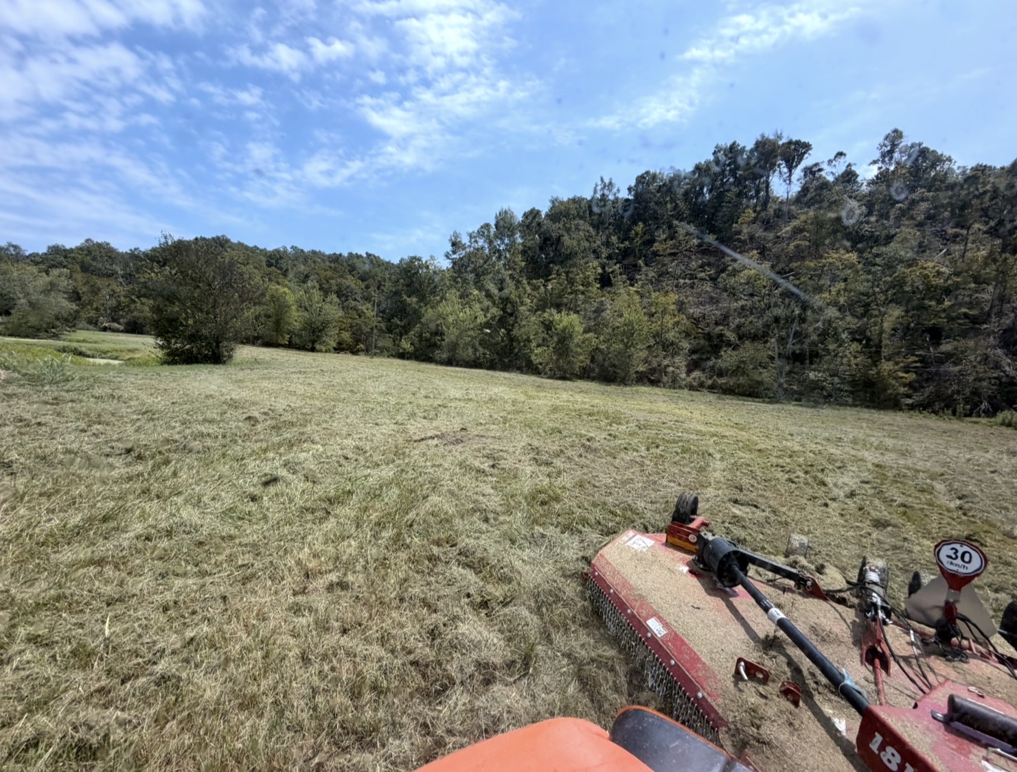 Brush hog mowing a large field under a blue sky from the operator seat