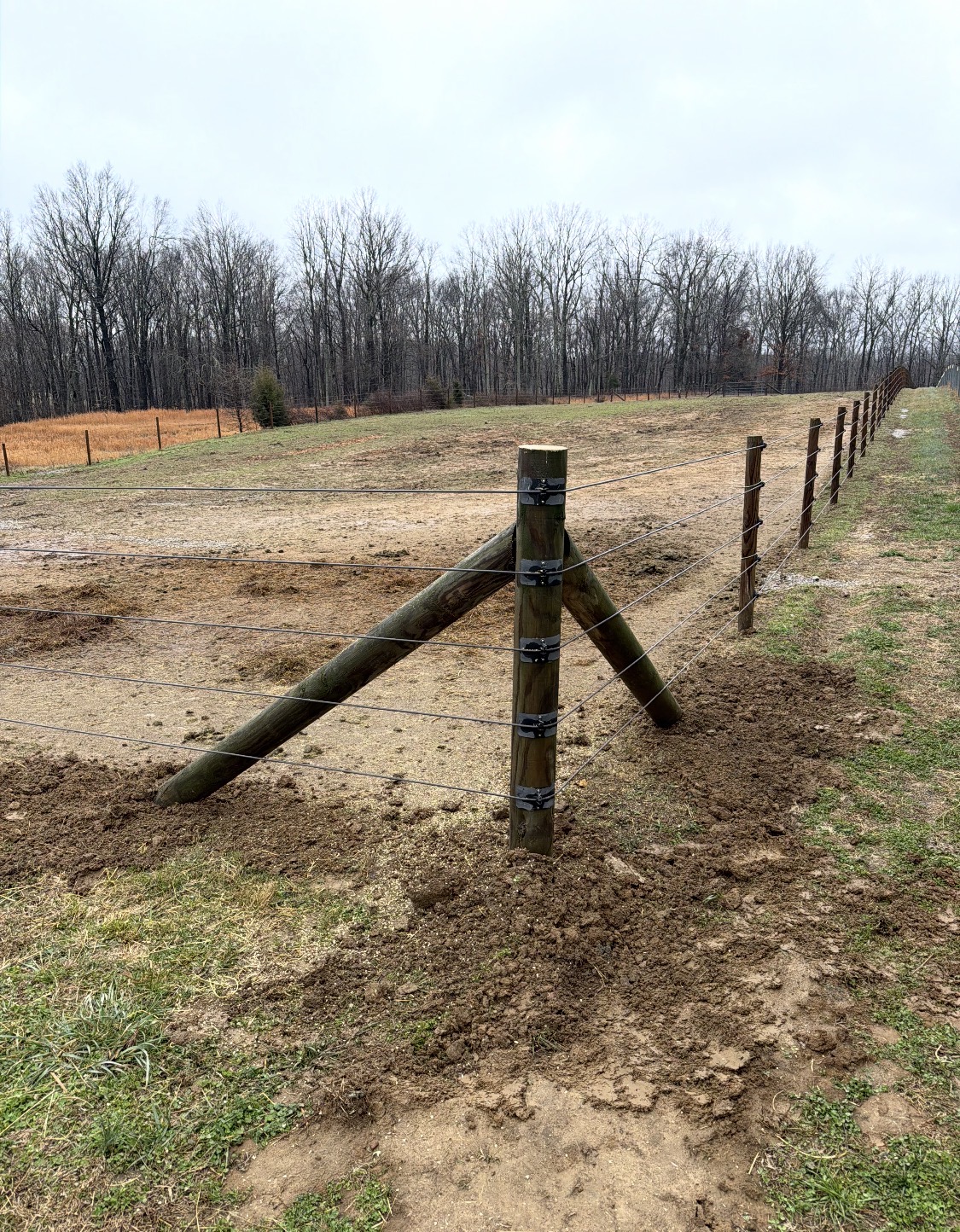 Repaired fence line with braced wood posts and wire across a field