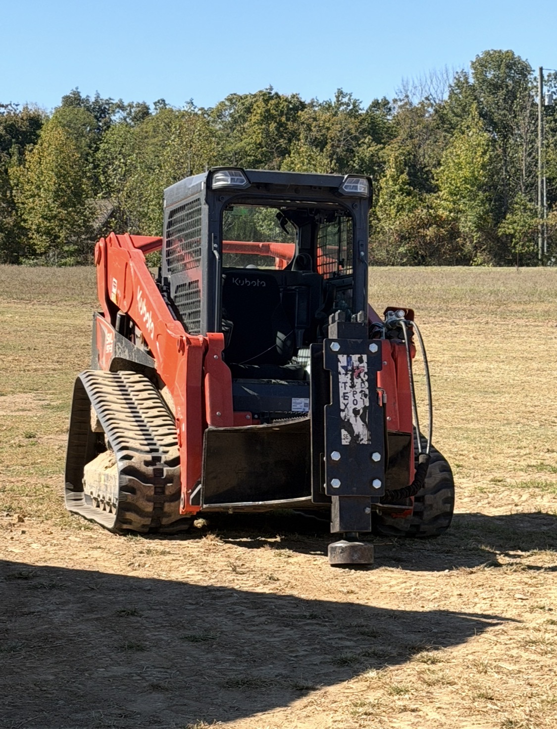 Kubota skid steer fitted with a post driver attachment in a field